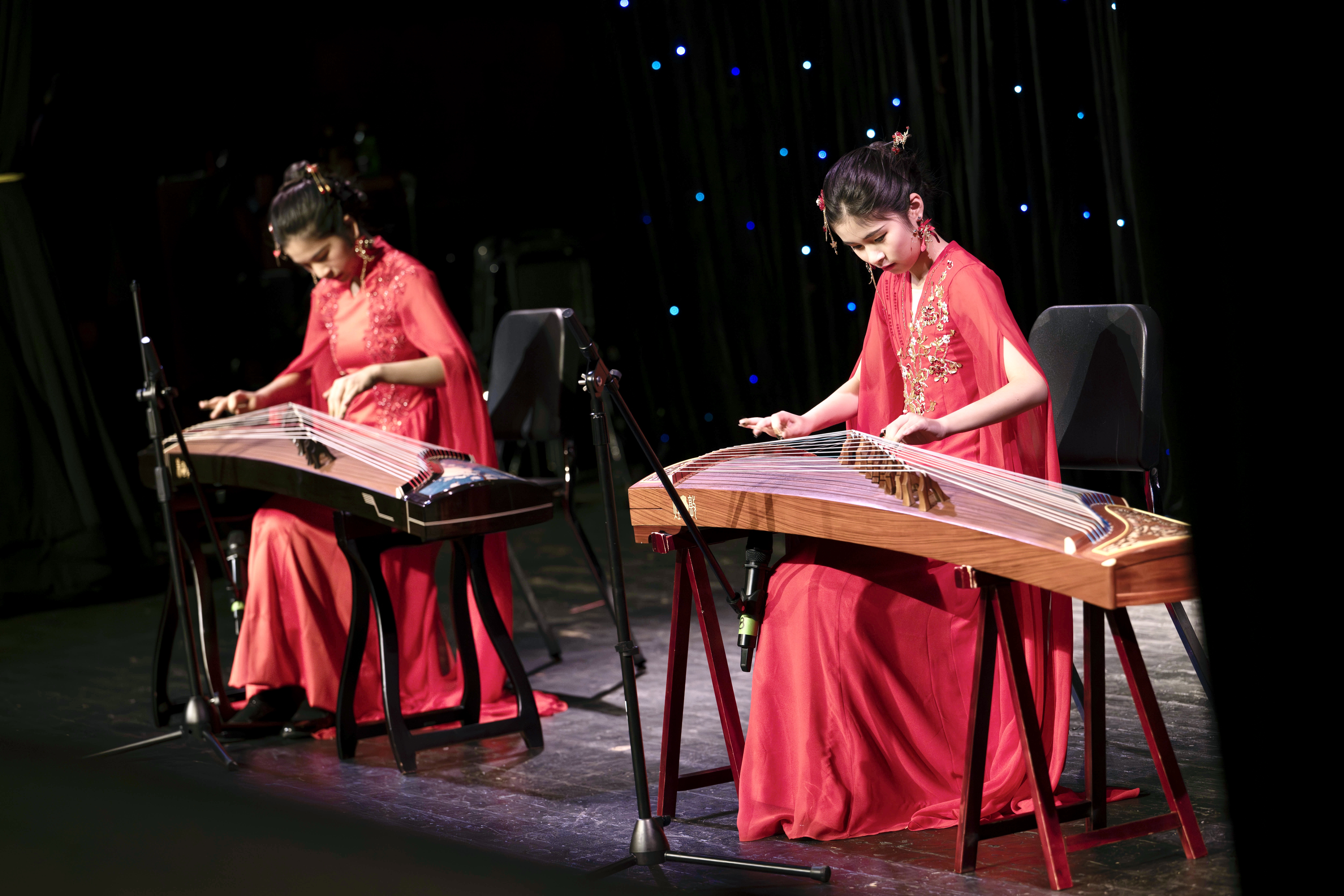 Three young girls in traditional Chinese hanfu performing on guzheng instruments on an elegant stage